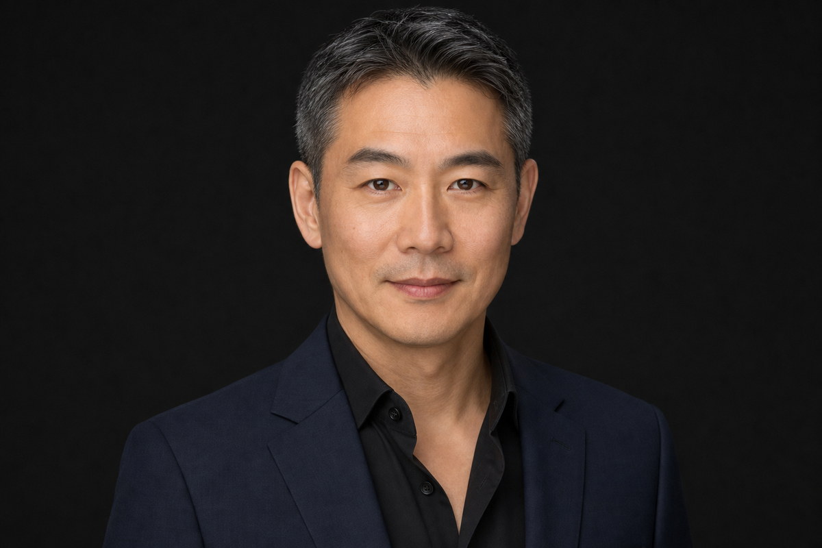 Professional studio headshot in a navy jacket against a dark background.