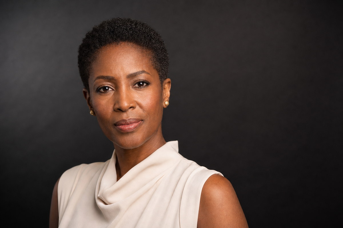 Professional studio headshot in a white sleeveless top against a dark background.