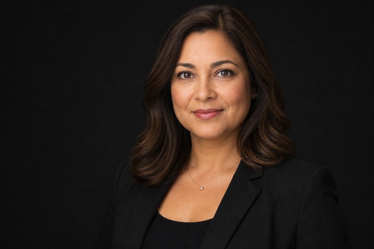 Professional headshot in a black blazer against a dark studio background.